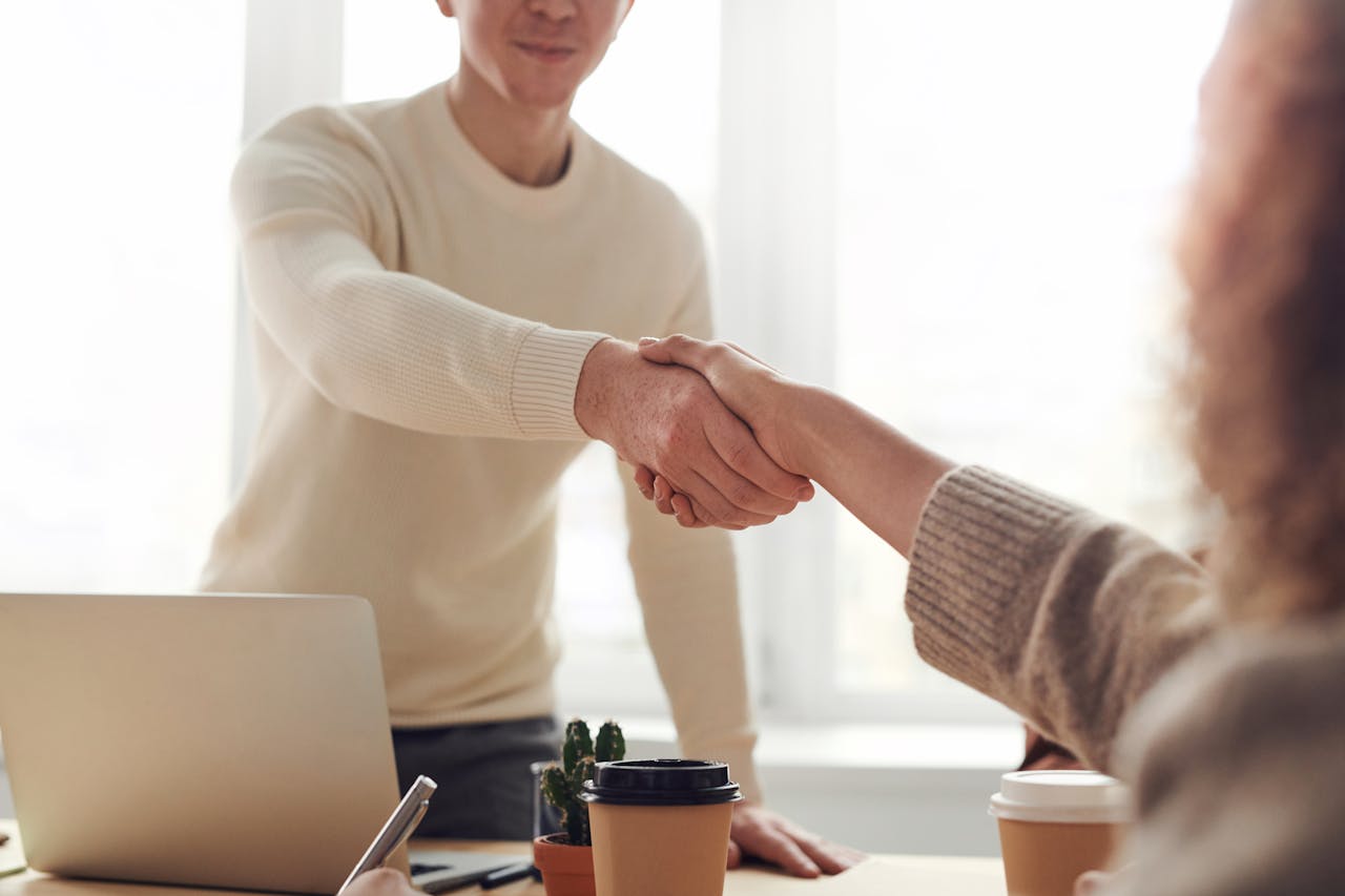 our-story Close-up of professionals shaking hands over coffee in a modern office.