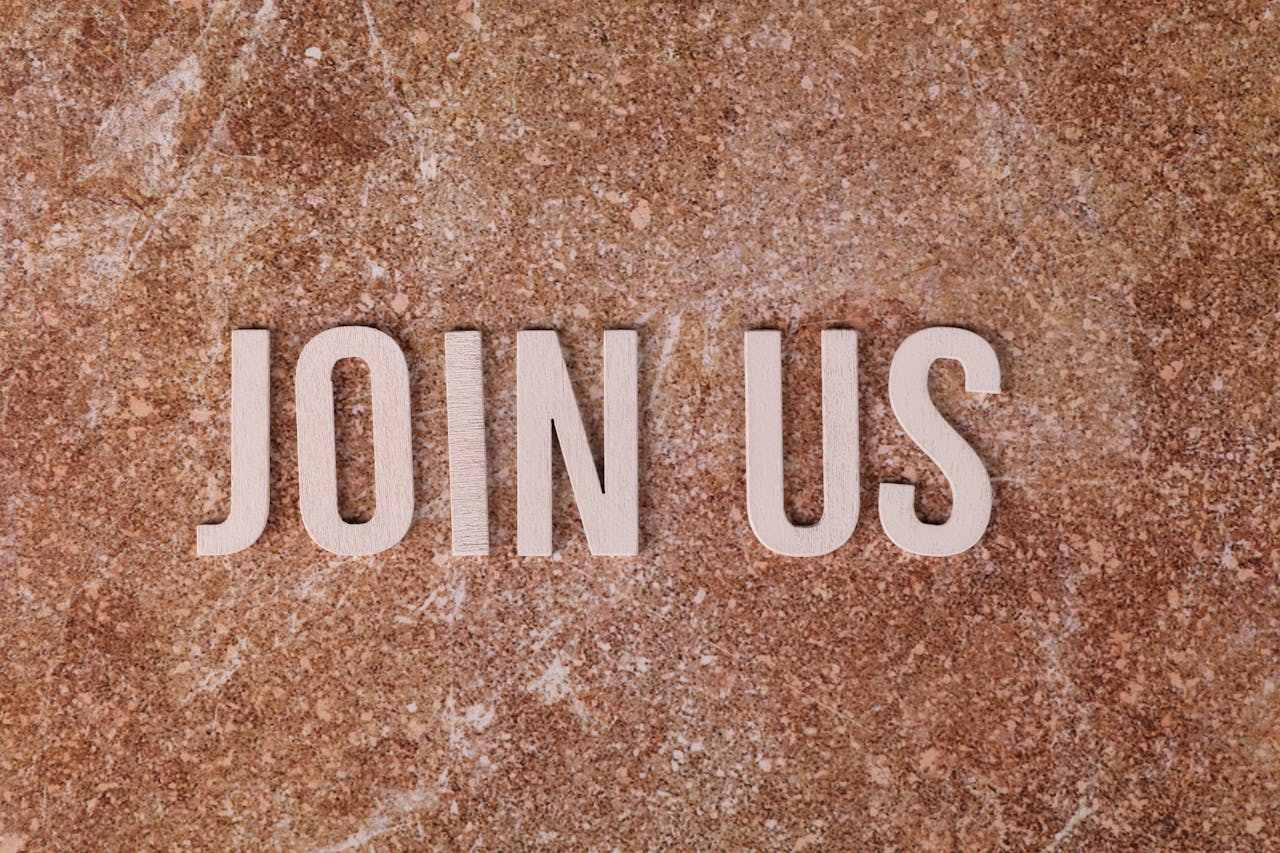 who-we-are Wooden letters spelling 'Join Us' on a brown textured surface, suitable for invitations.