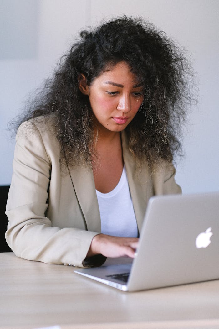 Mastering the First Impression: Your intriguing post title goes here Young ethnic female in stylish outfit sitting at table and browsing laptop while working in office