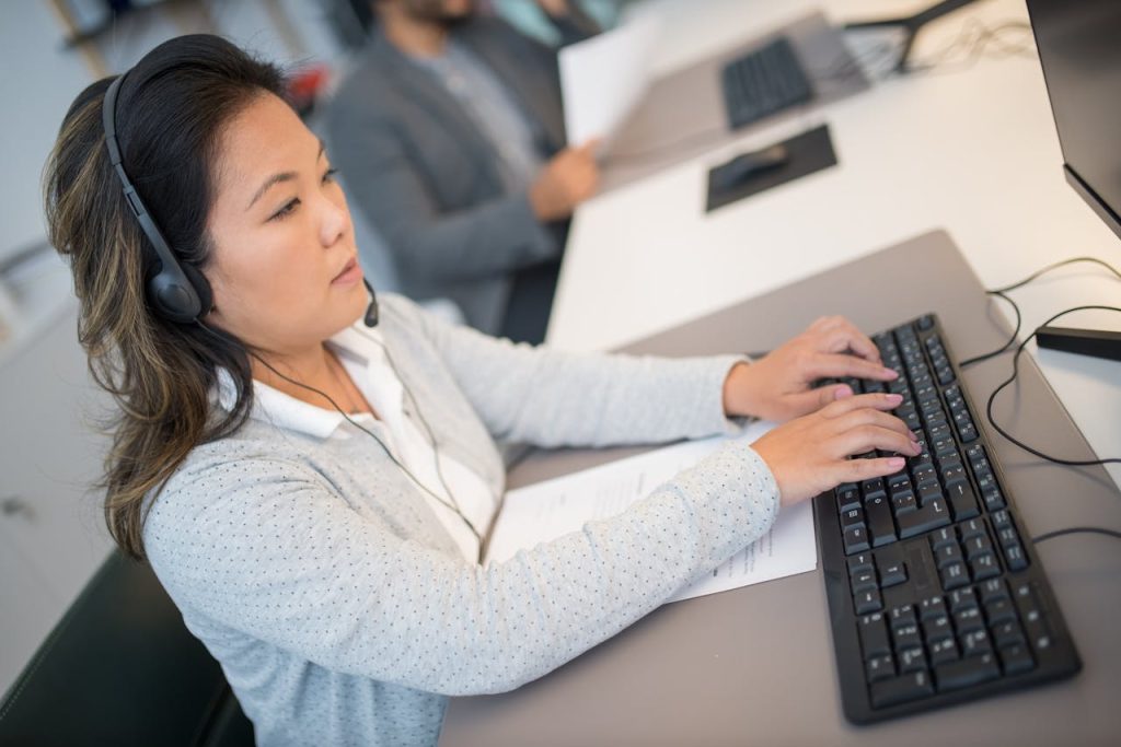 pexels photo 8204361 Asian woman working at a computer with headphones in a modern office setting.